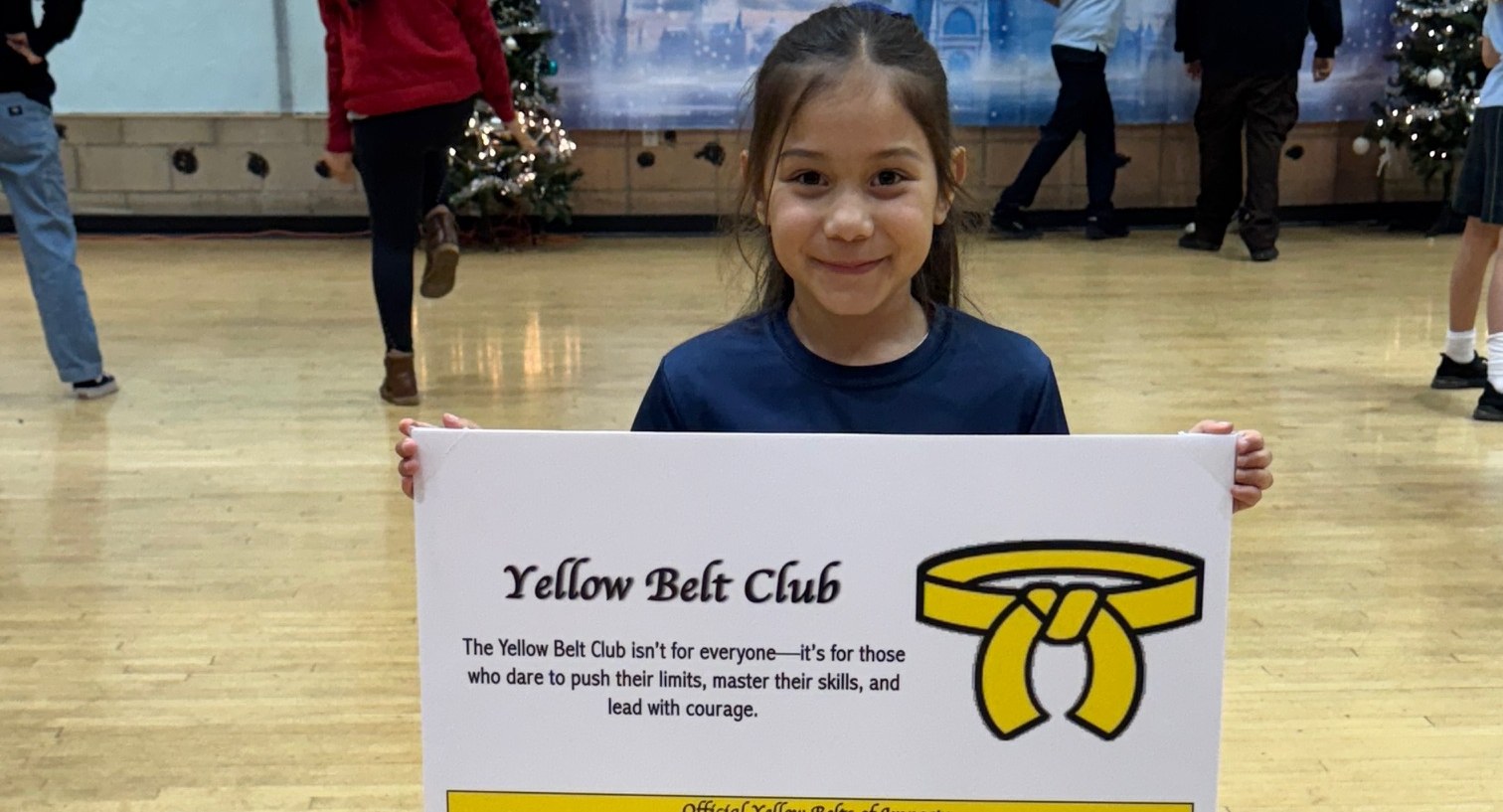 A student holding the Yellow Belt Club board after earning her place on it